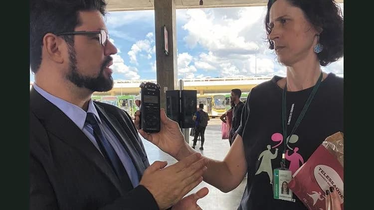 Dr. Mário Guimarães, de terno, sendo entrevistado por repórter da Rádio Câmara com gravador em punho na Rodoviária do Plano Piloto, em Brasília, fevereiro de 2023