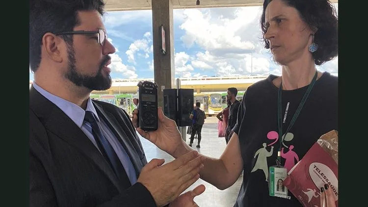 Dr. Mário Guimarães, de terno, sendo entrevistado por repórter da Rádio Câmara com gravador em punho na Rodoviária do Plano Piloto, em Brasília, fevereiro de 2023